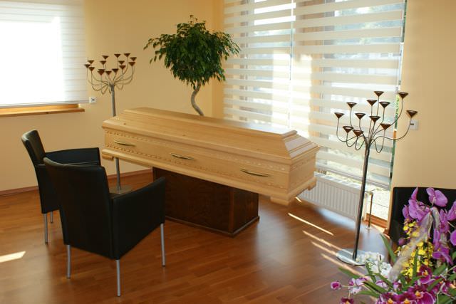 Heller Sarg im Verabschiedungsraum, davor zwei Sessel, daneben Kerzenleuchter und Orchideen